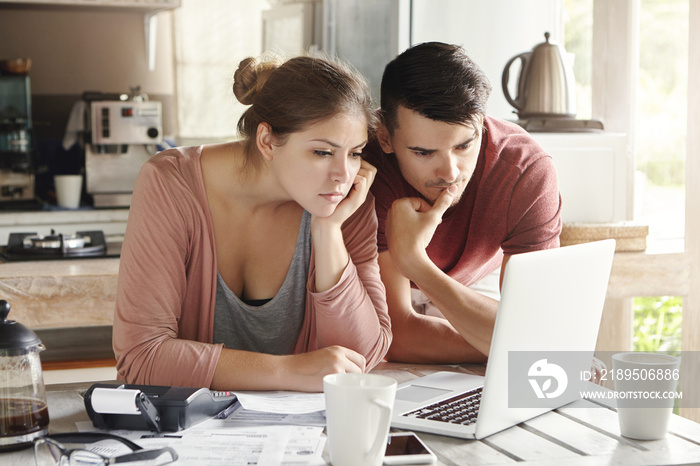 Young man and woman working together on laptop, paying utility bills via internet or using online mo