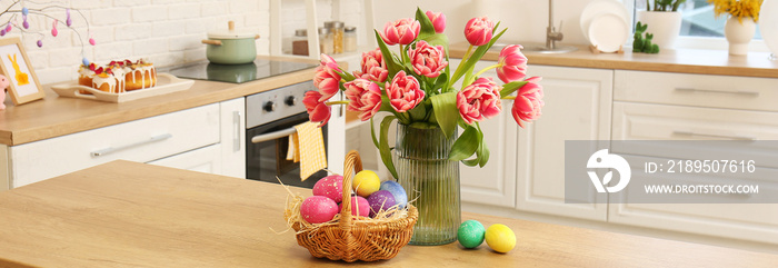 厨房桌子上放着一篮复活节彩蛋和一个花瓶，上面有新鲜的郁金香
