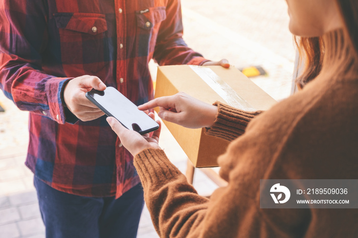 woman receiving parcel box and signing name on the phone from delivery man at the houses door