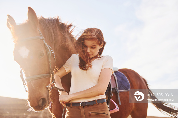 美丽的阳光。年轻的女人白天和她的马站在农田里