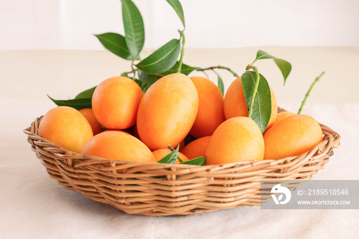 Big size fresh ripe organic sweet yellow marian plum or plum mango in wood basket on table. Tropical