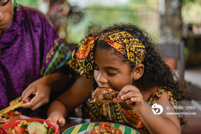 Imagen horizontal de una niña afrocaribeña disfrutando de un delicioso trozo de pollo caribeño senta
