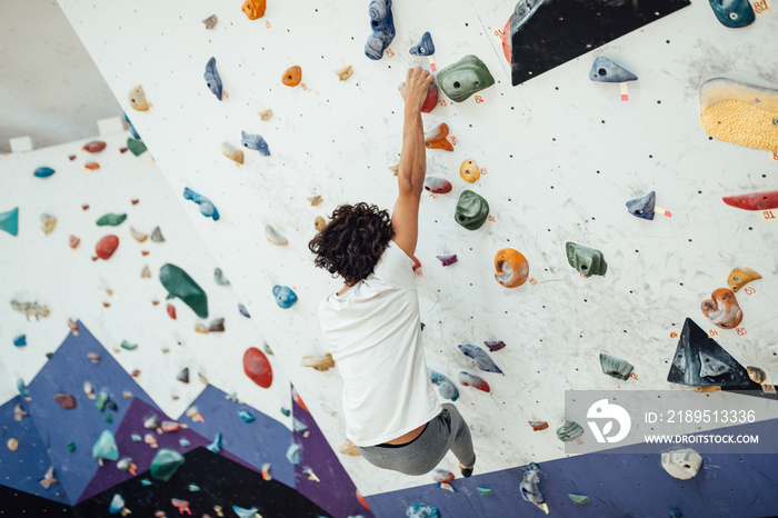 Strong man practicing rock-climbing indoors on a rock wall.