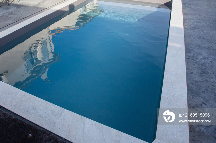 modern home swimming pool with stone coping with grey waxed concrete terrace and blue transparent wa