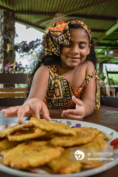 Imagen vertical de una hermosa niña afrocaribeña muy sonriente disfrutando de unos deliciosos pataco