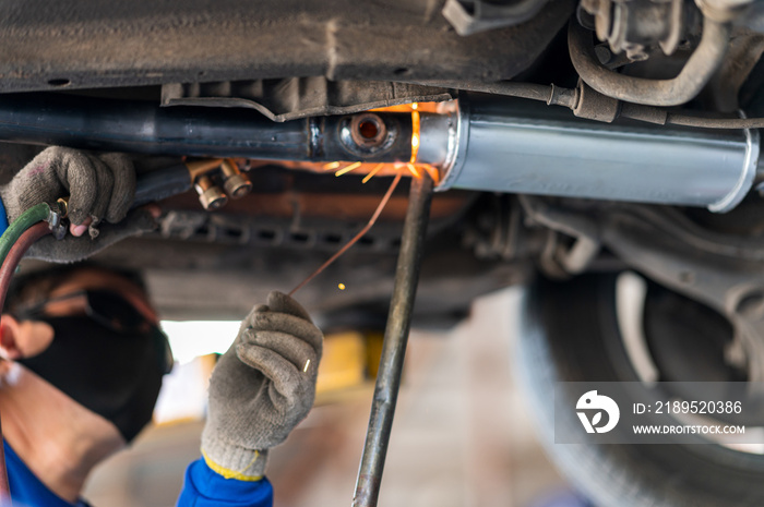 The mechanic is welding the car exhaust pipe.