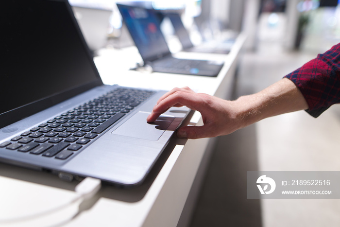 The man controls the computer with a touchpad. A mans hand uses a laptop in the electronics store. 