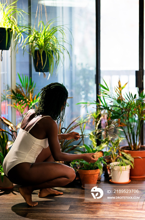 Black woman with green dreadlocks caring for her plants in her house