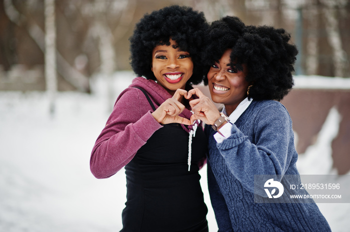 两个卷发的非裔美国女人在冬天穿毛衣摆姿势，用手指展示爱心。