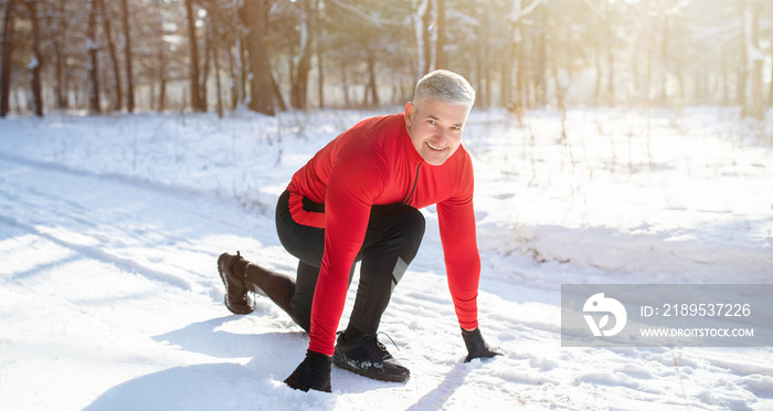 Outdoor winter activities. Mature sportsman getting ready to run marathon on snowy road on cold sunn