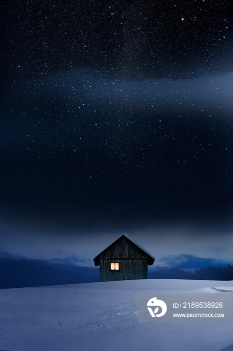 Blockhaus mit Leuchtendem Fenster im Winter bei Dämmerung