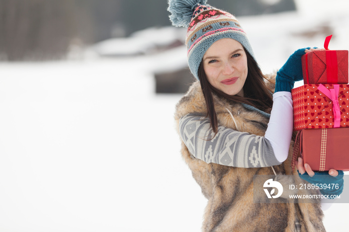 Portrait happy young woman carrying Christmas gifts in snow