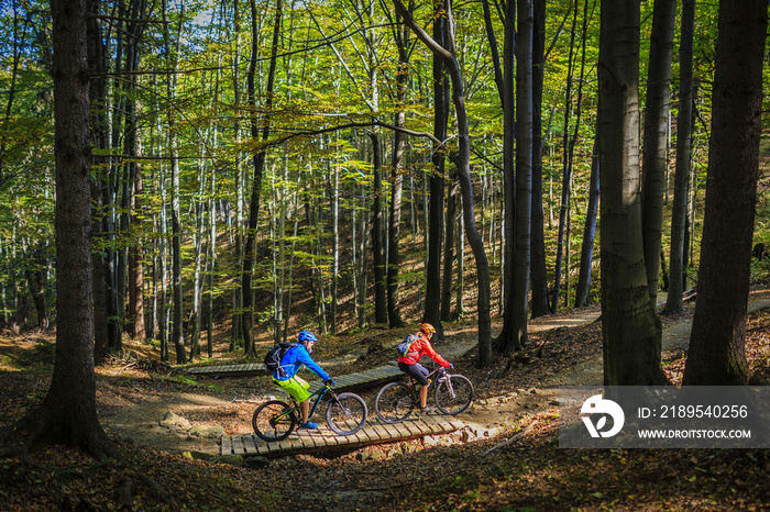 Mountain biking women and man riding on bikes at sunset mountains forest landscape. Couple cycling M