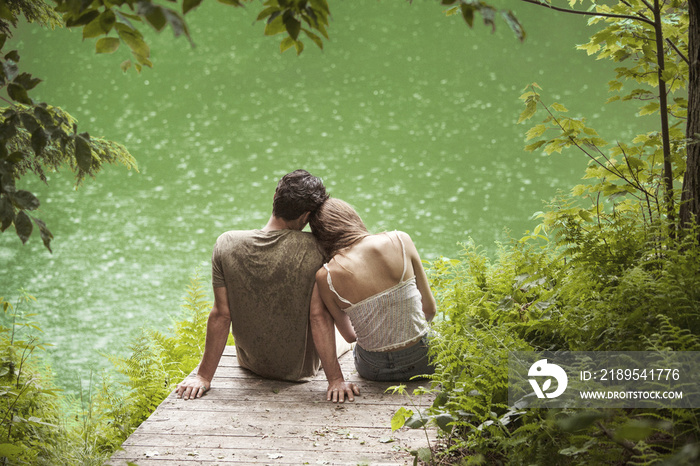 Rear view of couple relaxing on pier at lakeshore