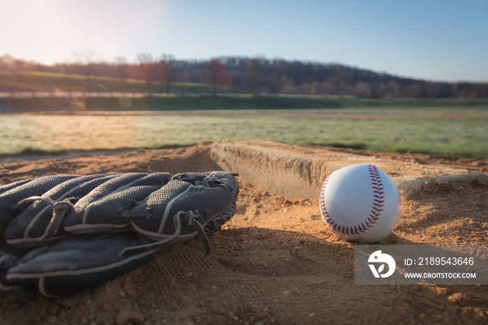 棒球手套和棒球在投手丘上，背景是太阳升起