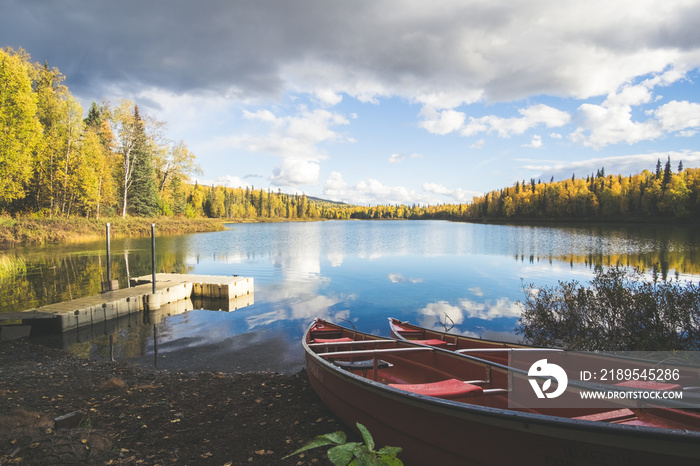 塔基特纳湖上的码头和两艘红色独木舟，开阔的湖面，秋天的树木和云朵的倒影。