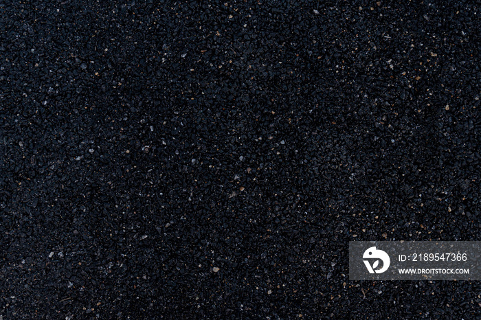 Background and textured of image of an asphalt surface that overlooks a mixture of rock and black ru