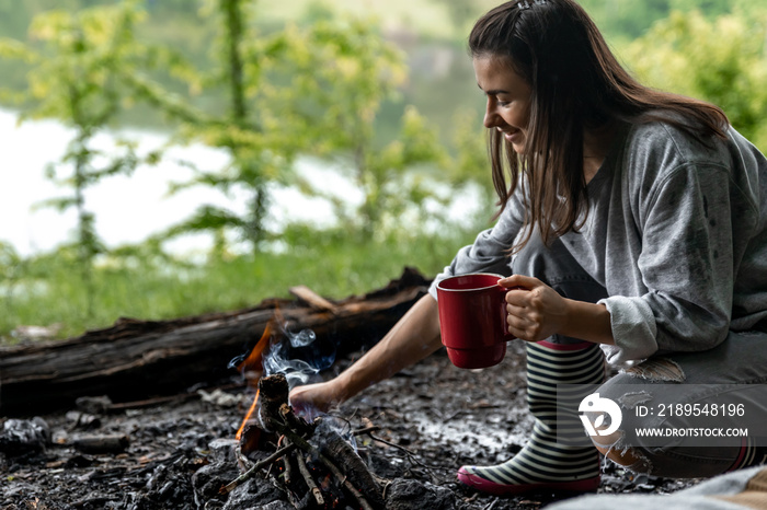 Girl with a cup of hot drink near the fire in nature.