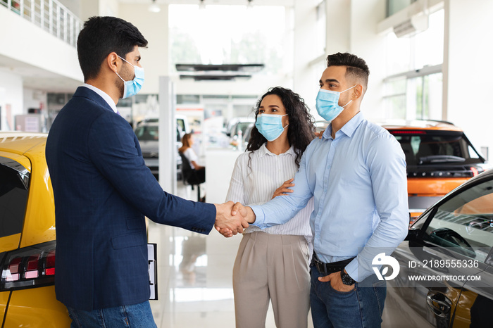 Middle-eastern couple shaking salesman hand, buying new car