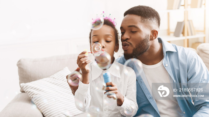 Handsome man spending time with daughter, blowing soap bubbles together