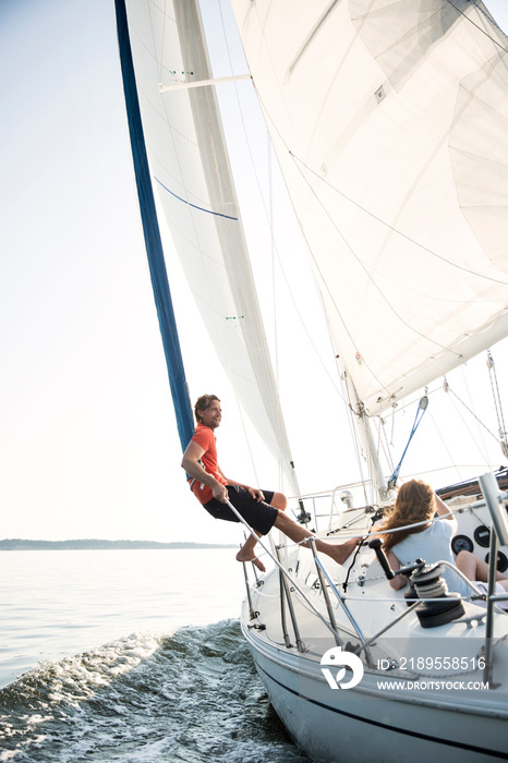 Man relaxing off edge of sail boat with friends