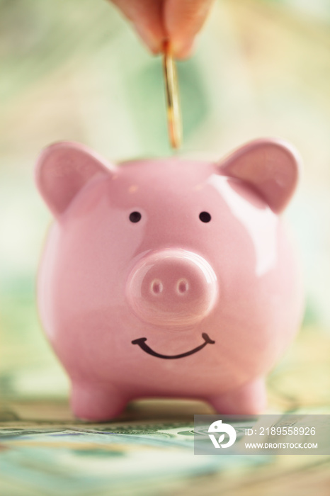 将金币存入微笑的粉红色小猪银行，放在成堆的钱上。省钱的概念。
