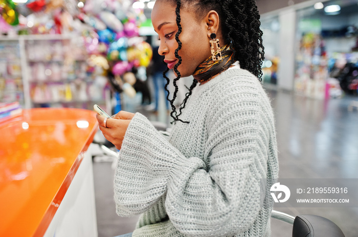 African woman bloger posed in sweater and jeans posed at mall with her mobile phone.