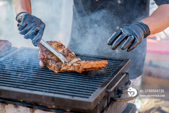 BBQ ribs. Hands in gloves overtake fried ribs on the grill