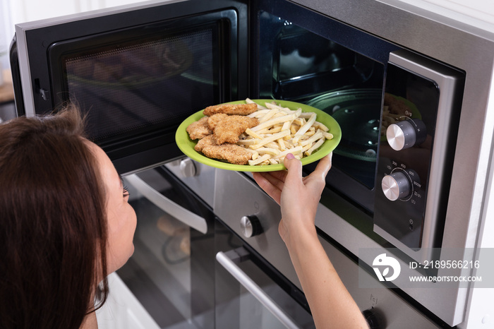 Woman Heating Fried Food In Microwave Oven