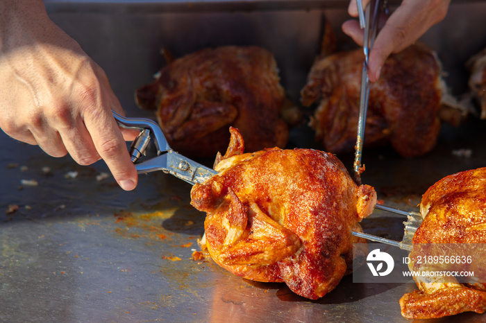 At a stall on a Spanish weekly market, chicken is prepared. The seller takes it from the spit. They 