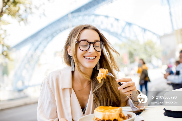 一位女士坐在餐厅里吃着传统的葡萄牙三明治，里面有一种名为francesinha的肉