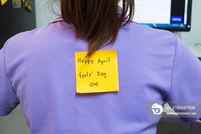 年轻女性办公室后面，贴着一张黄色的便签，上面写着踢我。四月快乐