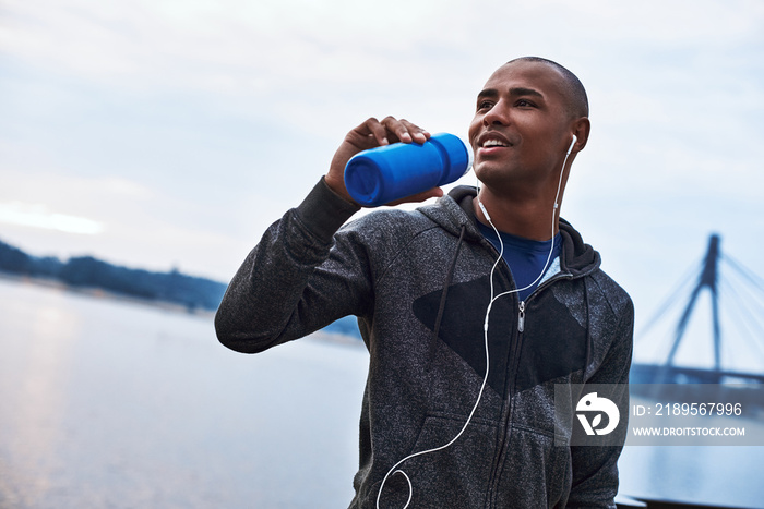 年轻的黑人运动员慢跑后正在喝蓝色瓶子里的水