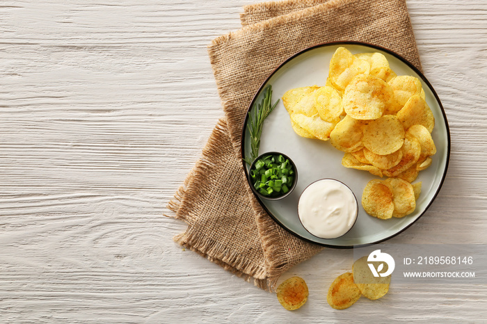 Plate with tasty sour cream, green onion and potato chips on table