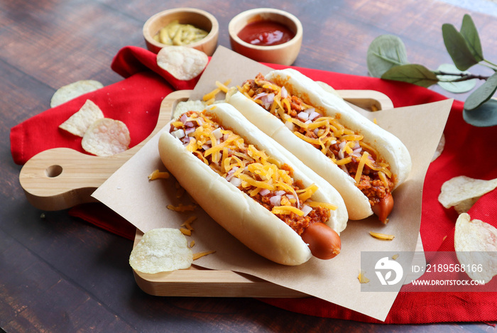 Chili dog, chili cheese hotdog served on wood tray with chips - close up view of fast food