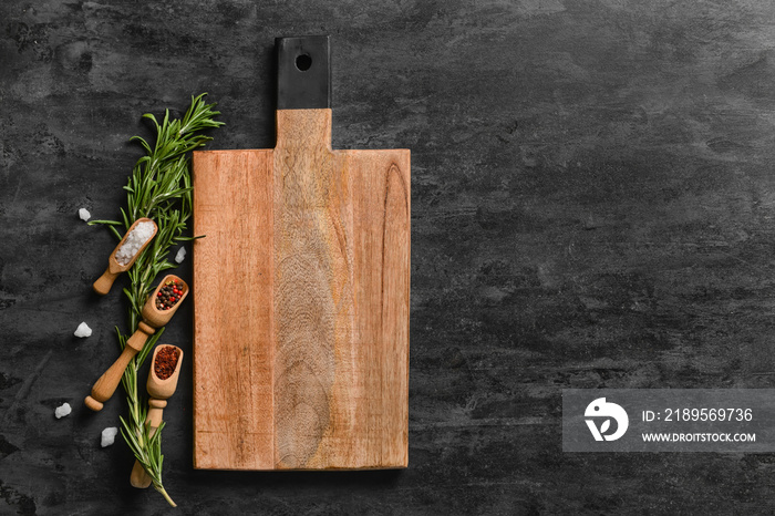 Wooden cutting board and spoons with spices on dark background