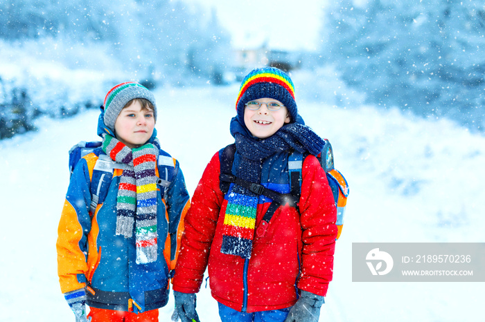 Two little kids boys of elementary class walking to school during snowfall. Happy children having fu