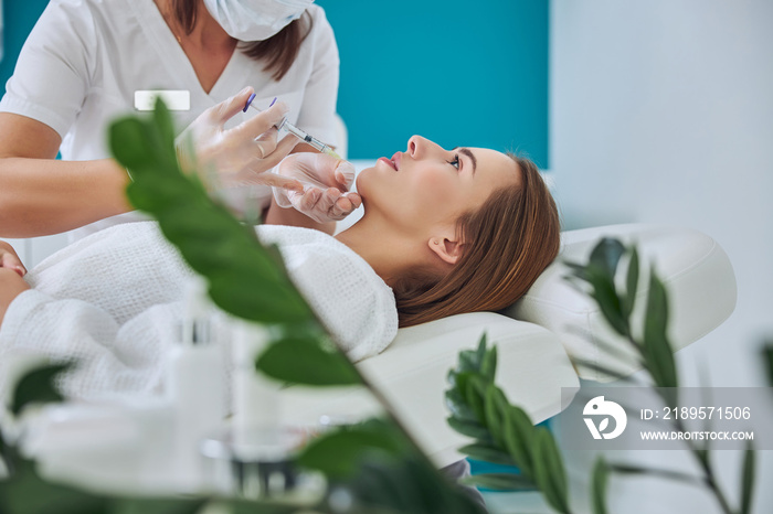 Elegant pretty female in white bathrobe getting beauty injection