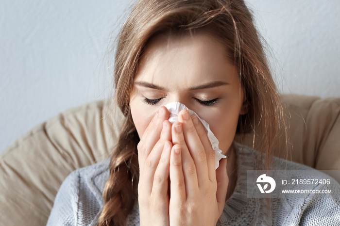 Young ill woman with tissue sitting on lounge at home