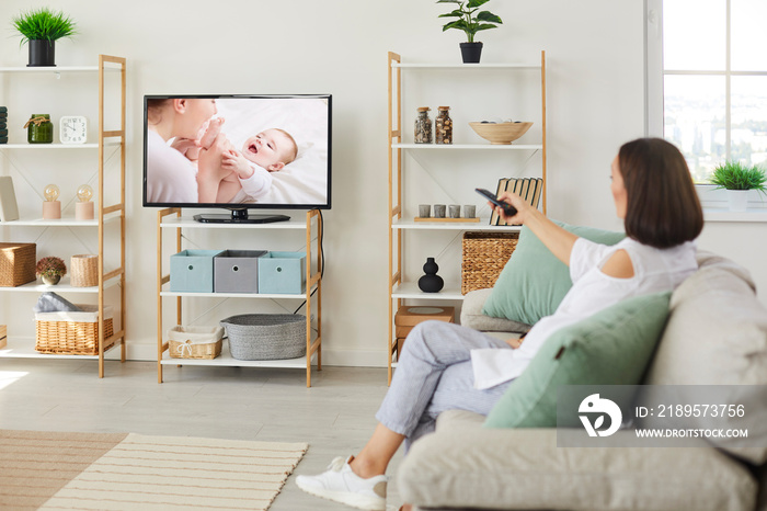 Woman sitting on sofa at home and watching movie on television. Happy relaxed adult lady resting on 