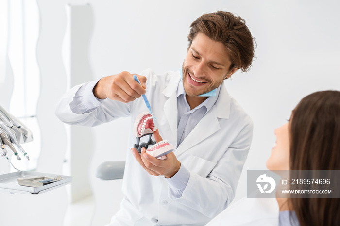 Handsome dentist showing how to brush teeth on jaw model