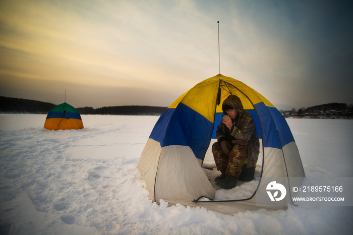 一名男子坐在雪地上的帐篷里喝酒