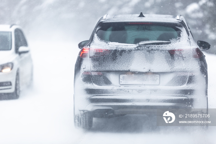 SUV car driving on snowy slippery road inside the forest, having registration number insivisible due