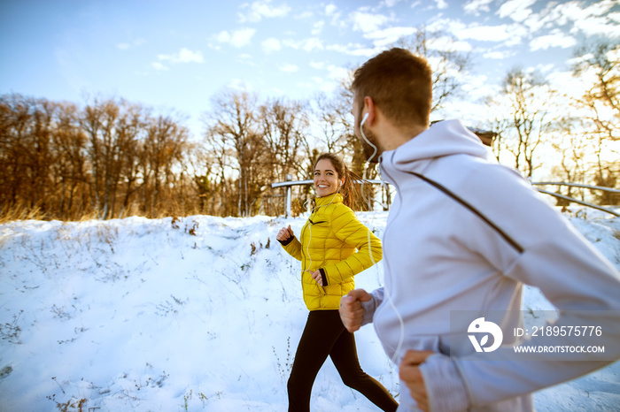 年，一对年轻迷人的健康跑步情侣戴着耳机在雪地上慢跑