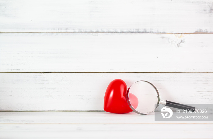 红色心形，白木背景上有放大镜。寻找爱情或健康的象征