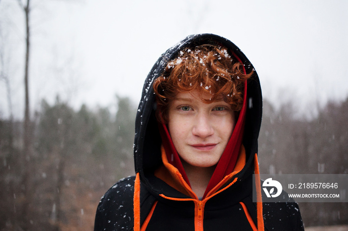 降雪期间戴着兜帽的男孩站在天空中的肖像