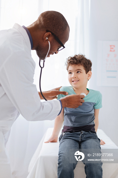 Chest examination. Smart skillful male doctor standing while using stethoscope and hearing boy