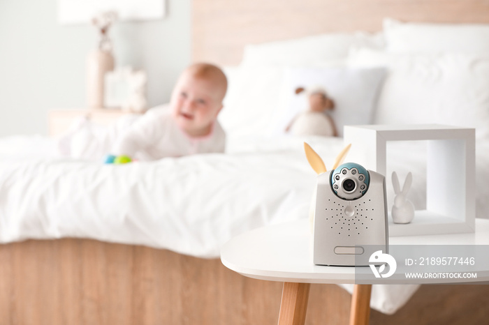 Modern baby monitor on table in room with little child