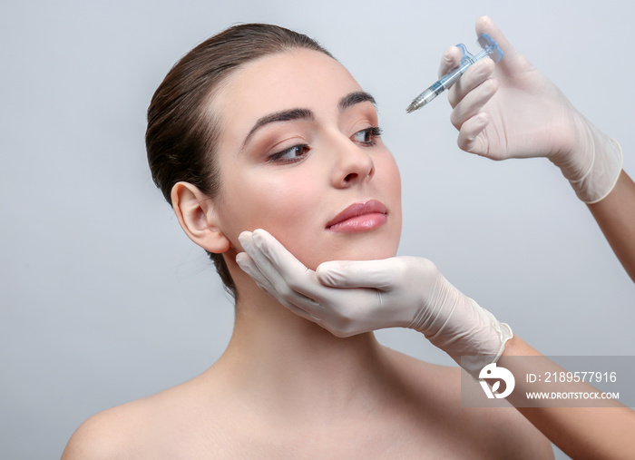 Beautiful young woman receiving filler injection in face, on light background