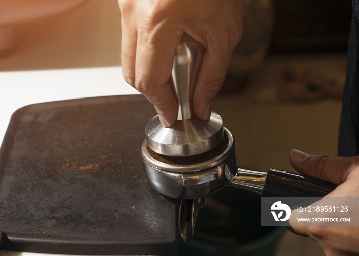 Close-up Barista pressing ground coffee into portafilter by tamper to making coffee